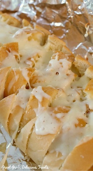 Pull Apart Garlic Cheese Bread - photo of a French loaf of bread with cuts diagonally and stuffed with melted mozzarella cheese, placed on a piece of foil.