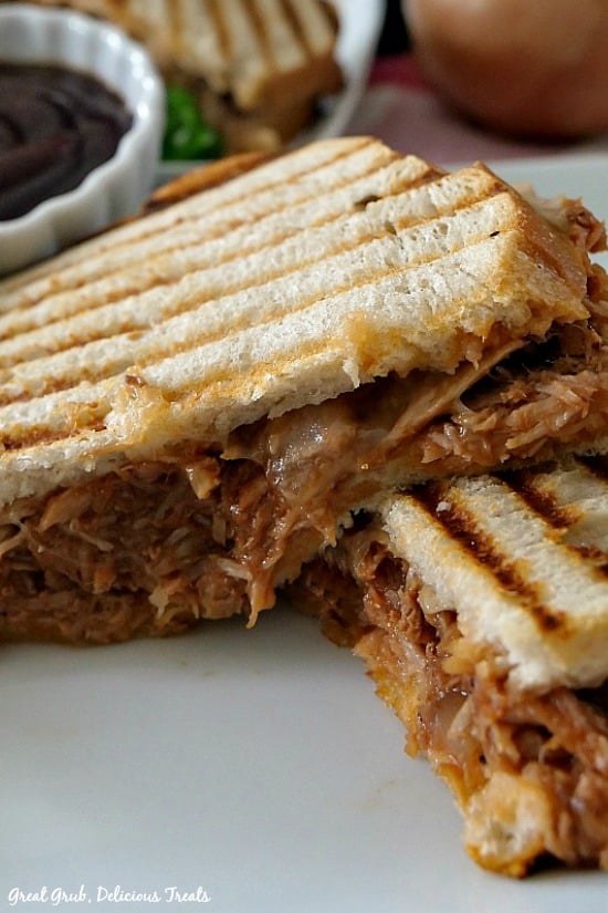 Two halves of a BBQ pulled pork panini sandwich with a small white bowl filled with barbecue sauce in the background.