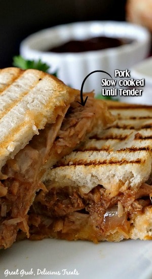 A close up photo of BBQ pulled pork panini, with sandwich cut in half and stacked on one another, with a small white bowl of BBQ sauce in the background.