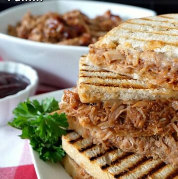 BBQ panini sandwich on a white plate with a white bowl of pulled pork in the background.
