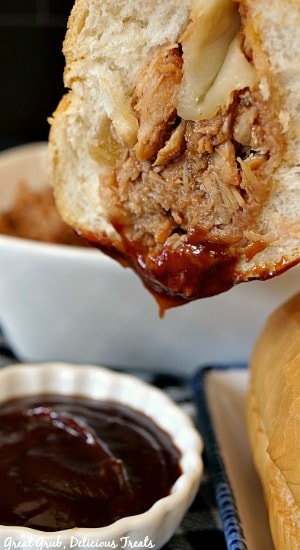 A close up photo of a BBQ Pulled Pork Hoagie dipped in barbecue sauce with a small white bowl full of barbecue sauce in the foreground.