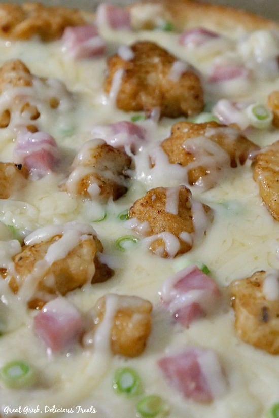 Chicken Cordon Bleu Alfredo Pizza - a close up photo of the pizza coming right out of the oven with melted cheese, breaded fried chicken pieces, diced ham, green onions atop of Alfredo sauce.