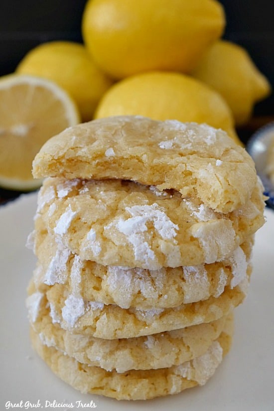 Lemon crinkle cookies stacked 6 high on a white plate with lemons in the background.