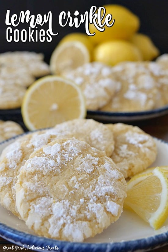 Lemon crinkle cookies on a white plate with blue trim with lemons in the background.
