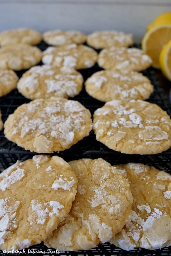 Lemon crinkle cookies layered on a black wire rack with lemon halves in the background