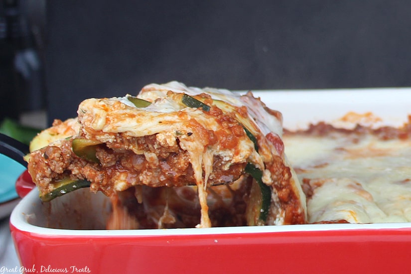 Zucchini Lasagna is a hearty, delicious, cheesy twist from the classic lasagna recipe, loaded with meat, 3 cheese and a delicious sauce and zucchini in place of the pasta. Red baking dish with a spatula full of zucchini lasagna being dished out of the baking dish.