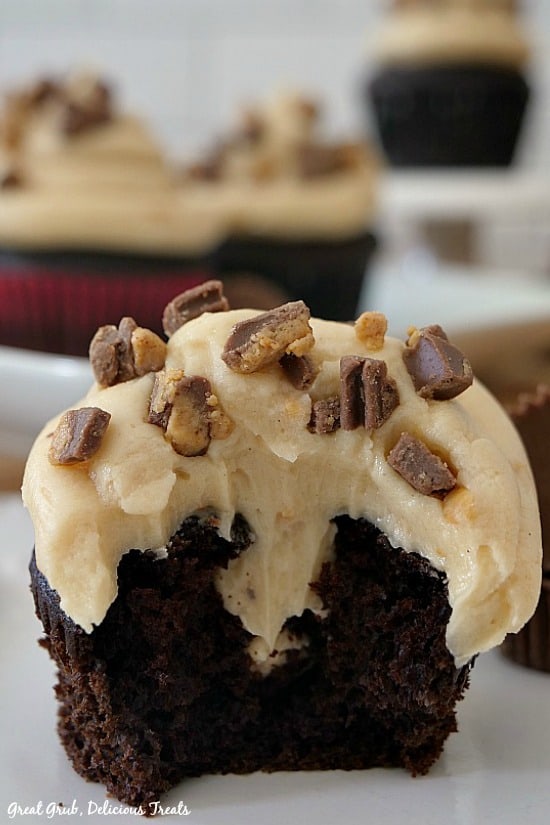 A close up photo of a chocolate cupcake with peanut butter frosting with a bite taken out showing the peanut butter stuffed center.