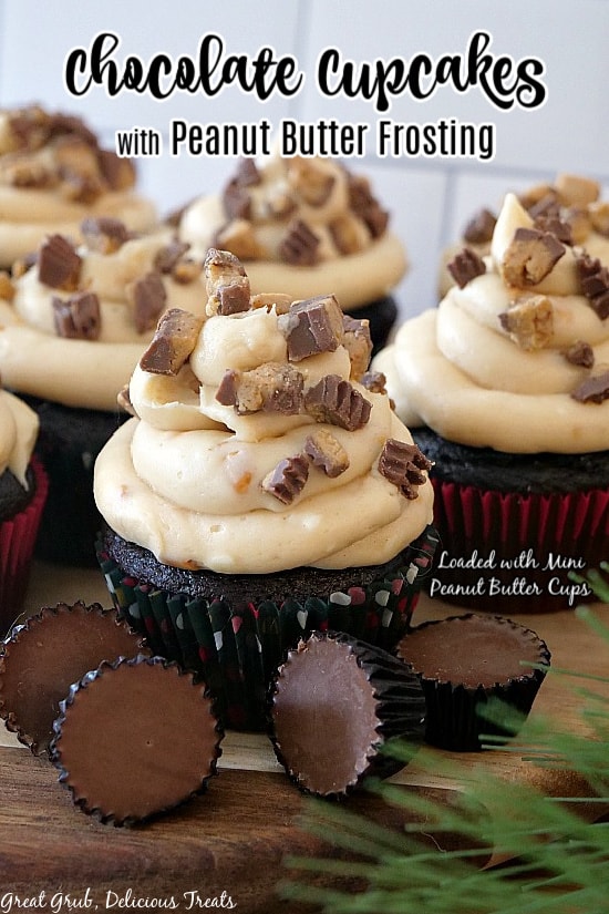 Chocolate cupcakes with peanut butter frosting on a wood surface with mini peanut butter cups placed in front of the cupcakes.