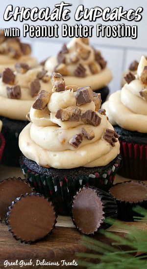 Chocolate cupcake in a polka dot liner, topped with peanut butter frosting, chunks of peanut butter cups, with cupcakes in the background, and peanut butter cups in the foreground.