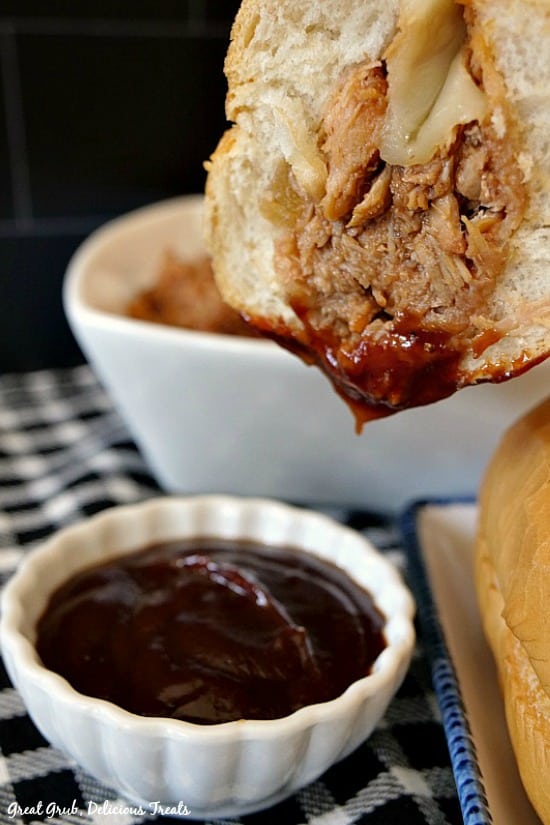 Close up picture of a BBQ pulled pork hoagie dripped in barbecue sauce, with a small white bowl filled with barbecue sauce in the foreground. 