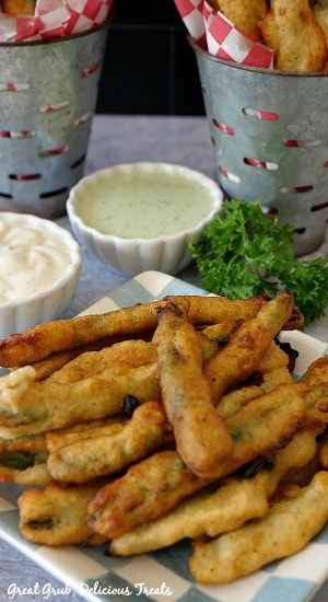 Fried Green Beans on a white and blue checkered plate with parsley and dipping sauces in the background.