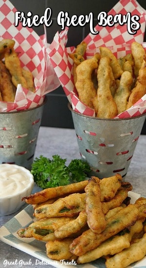 Fried Green Beans on a white and blue checkered plate with dipping sauce, parsley, and galvanized containers holding more fried green beans in the background with the title at the top.