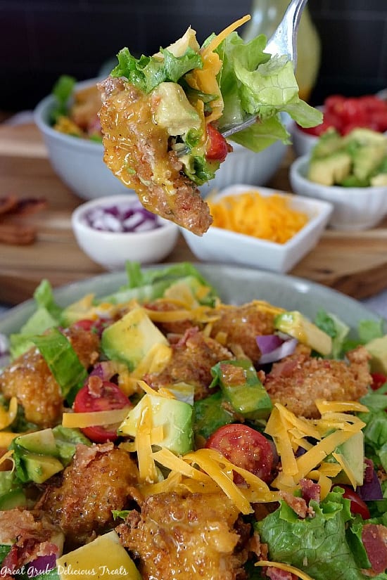 Close of photo of a bite of a crispy chicken salad on a fork with a bowl of salad in the background.