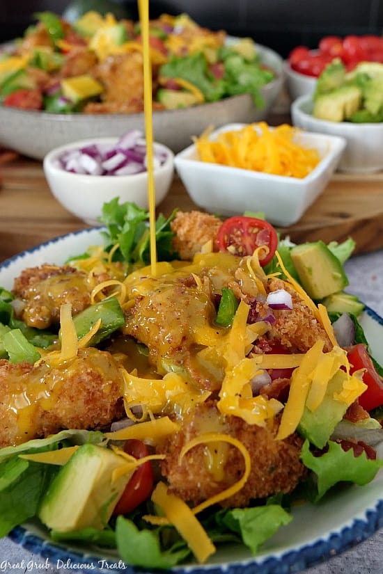 A white bowl with a blue rim full of crispy chicken salad with honey mustard dressing being poured on it.