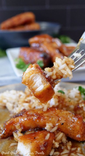 A fork with a bite of lemon honey glazed chicken and rice being held up over a serving of this chicken recipe.