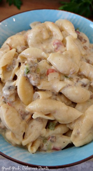 A close up photo of creamy Italian sausage pasta in a blue bowl with parsley in the background.