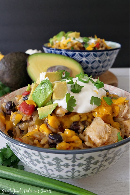 Two bowls filled with Southwest Chicken Bowls with chicken, rice, corn, bean and topped with diced avocados, sour cream, cilantro and cheese.