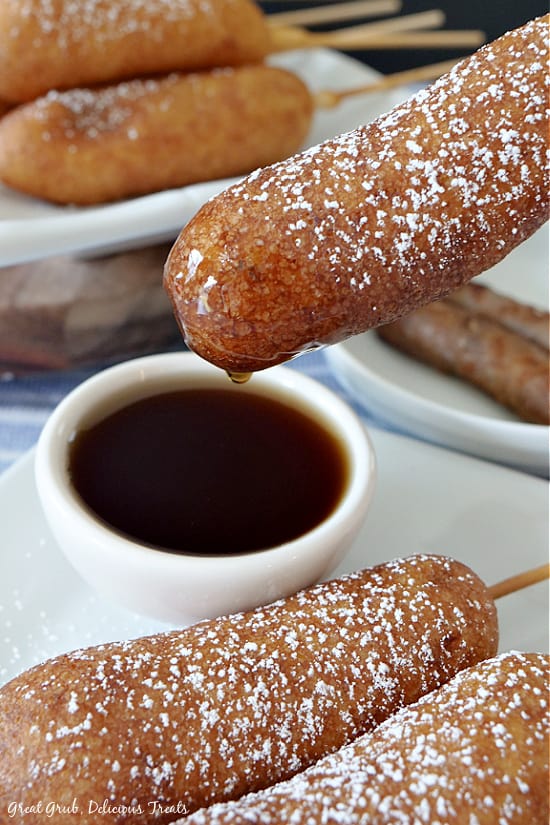 a Pancake Sausage on a Stick being dipped into maple syrup.