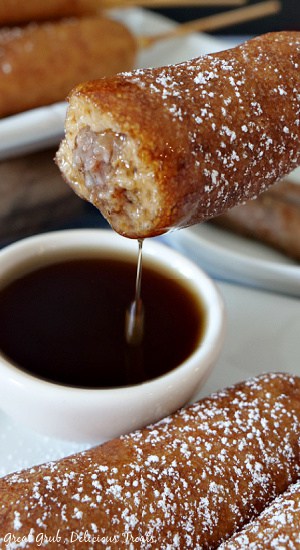 A pancake sausage on a stick with a bite taken out out and dipped in maple syrup.