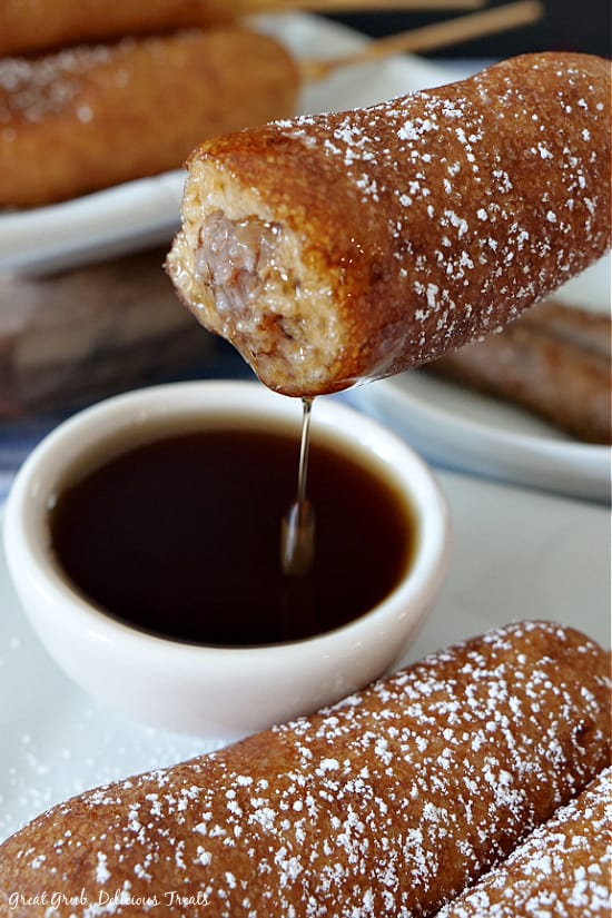 A Pancake Sausage on a Stick after a bite has been taken and after it has been dipped in syrup, showing the syrup dripping off the pancake on a stick.