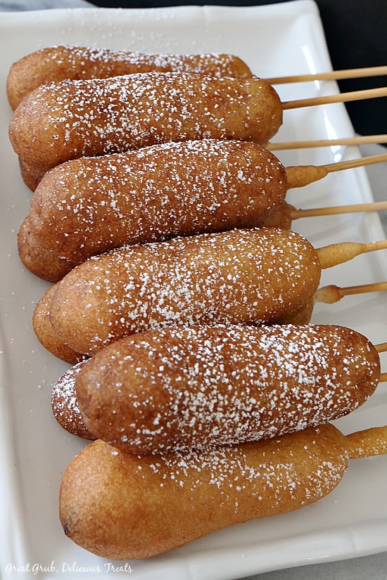 10 pancake sausage on a stick dusted with powdered sugar placed on a white oblong plate