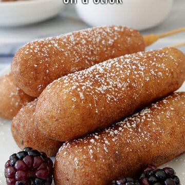 A close up photo of pancake sausage on a stick stacked on top of each other on a white plate with blackberries in the foreground.