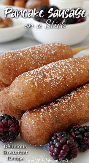 A close up photo of pancake sausage on a stick stacked on top of each other on a white plate with blackberries in the foreground. 