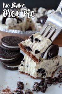 A photo of a slice of oreo pie with a bite on a fork, oreos on the left side for decoration, and the pie in the background.