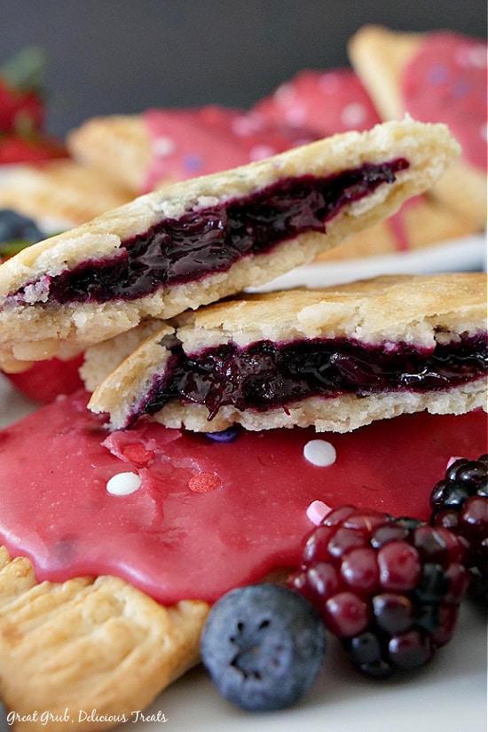 A homemade pop tart broke in half to show the fruit filling, then placed on top of another pop tart surrounded by blackberries and blueberries.