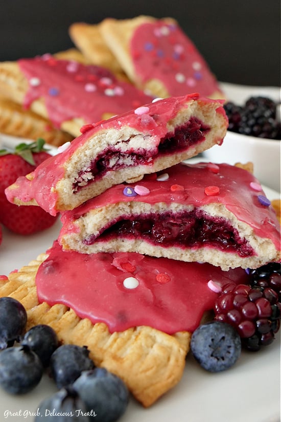 A photo of two homemade pop tarts with on broken in half showing the fruit filling with blueberries, blackberries and a strawberry placed around the pop tarts.