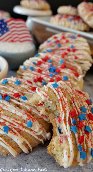 A stack of sugar cookies decorated with white chocolate and red, white and blue sprinkles and stars with more cookies on a white plate in the background.
