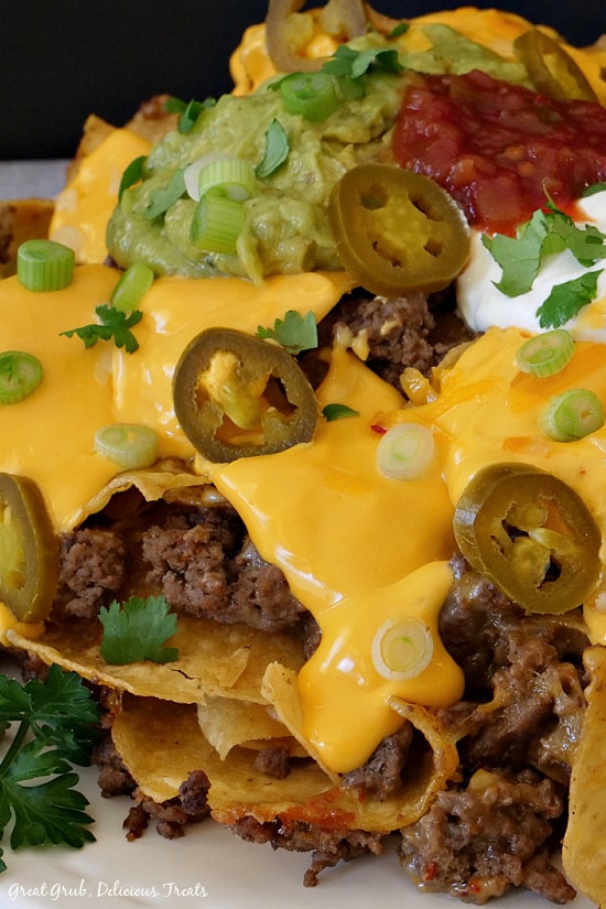 A close up picture of Mile High Nachos stacked up, showing ground beef, nacho cheese, green onion, guacamole, salsa. sour cream, jalapenos, and cilantro.