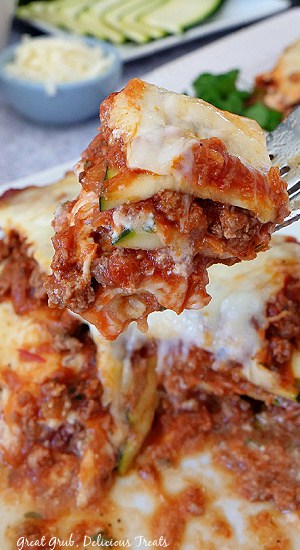 Zucchini Lasagna is a delicious lasagna recipe made without pasta and sliced zucchini for a healthier version of the classic lasagna recipe. A close up photo of a bite of zucchini lasagna on a fork being held above a serving of lasagna.