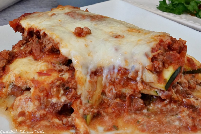Zucchini Lasagna is a hearty and cheesy comfort food recipe loaded with a delicious meat sauce, zucchini, and three types of cheese. A white plate with a serving of zucchini lasagna.