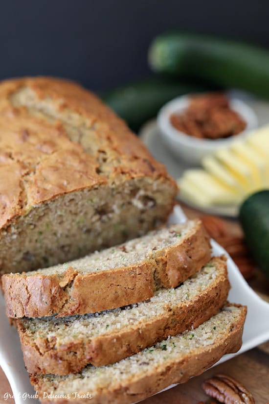 Zucchini Bread - a loaf of zucchini bread on a white plate with 3 slices cut ready to be served.