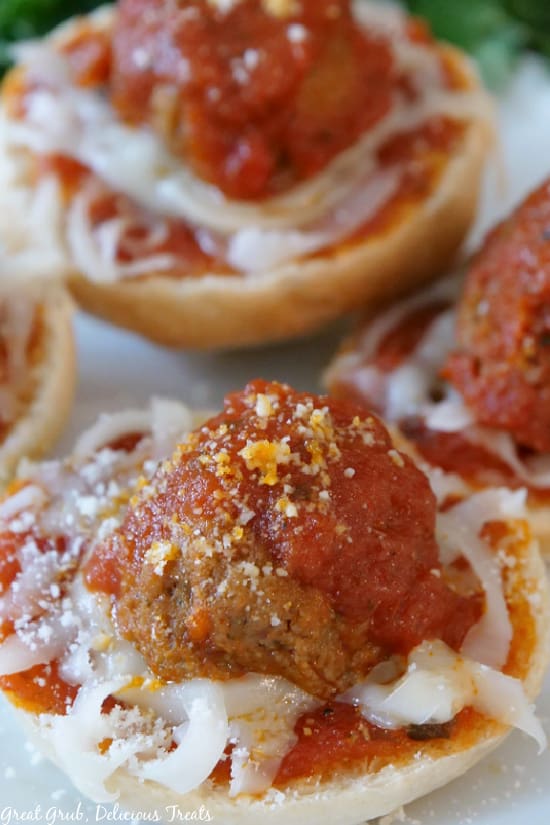 A close up picture of Meatball Bagel Bites on a white plate, showcasing the melted mozzarella cheese, cooked meatballs, tomato sauce, and parmesan cheese.