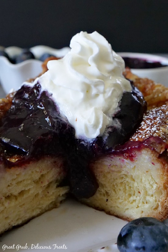 French Toast with Blueberry Topping is a delicious, thick and custardy French toast recipe that is fried to golden brown then baked until the custard is thoroughly cooked. A close up photo of a slice of French Toast with Blueberry Topping on a white plate.