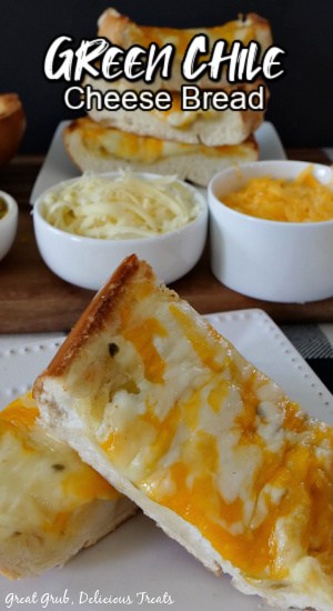 Two slices of Green Chile Cheese Bread on a white plate with shredded cheese in two small white bowls and more slices of cheese bread in the background.