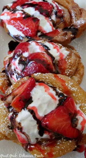 Three funnel cakes with strawberries and whipped cream on them.