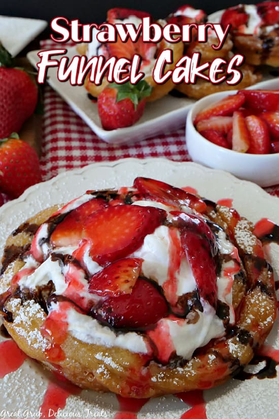 A funnel cake on a white plate, topped with powdered sugar, fresh strawberries, whipped cream, and chocolate syrup.