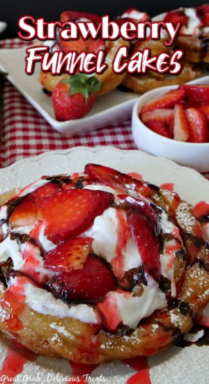 A funnel cake on a round white plate with strawberries, whipped cream and chocolate drizzle on it.