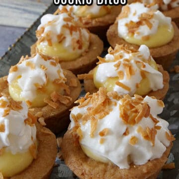 Coconut cream cookie bites sitting on a long silver tray, all topped with whipped cream and toasted coconut flakes.