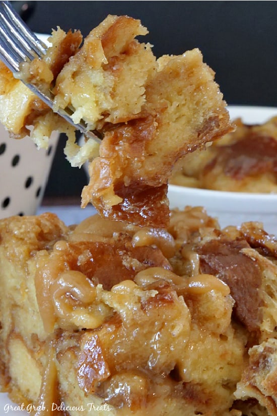 A forkful of Caramel Bread Pudding held up above a serving of bread pudding on a white plate.
