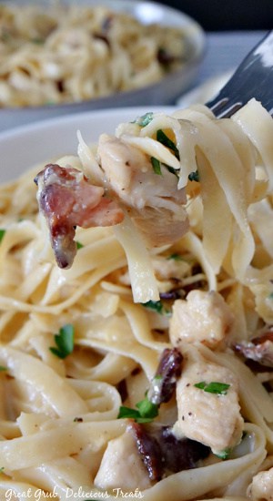 Chicken Carbonara is a delicious pasta recipe that is made with bacon, chicken, and coated in a mixture of eggs and parmesan cheese. A close up photo of chicken carbonara with a large bite twirled around a fork.