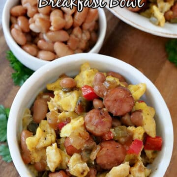 A white bowl on a brown cutting board, loaded with eggs, sausage, beans, and bell peppers.