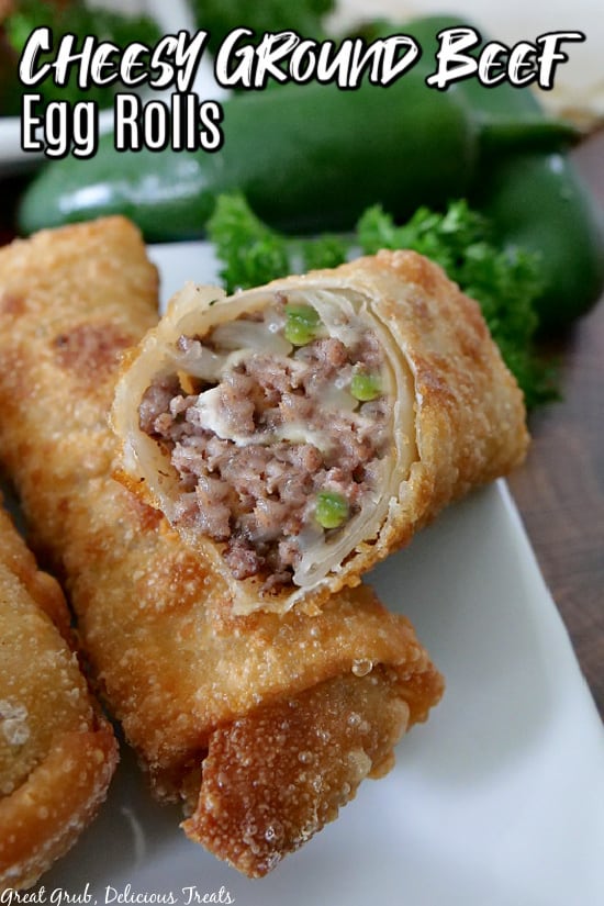 A white plate with 3 cheesy ground beef egg rolls on it with one showing the inside ingredients.