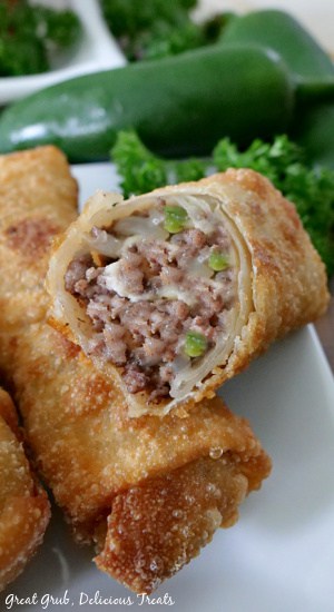 Three cheesy ground beef egg rolls on a white plate with one with a bite taken out showing the inside meat mixture.