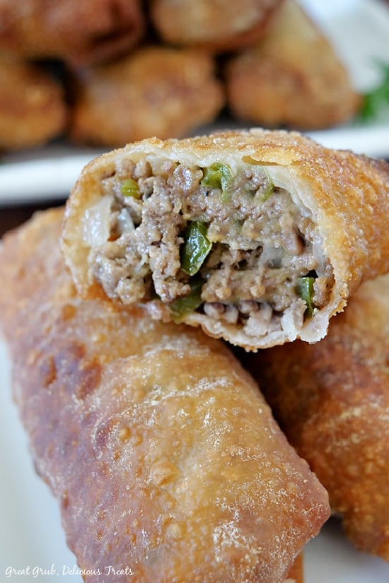 A cheesy ground beef egg roll, placed on top of two other egg rolls, with a bite taken out of it.
