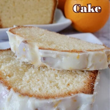 A white plate with 2 slices of pound cake on it, with half a loaf of orange pound cake and 2 oranges in the background.