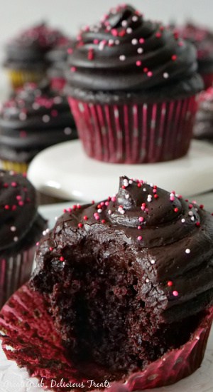A close up of a Dark Chocolate Zucchini Cupcake with a bite taken out of it with another cupcake on a small cupcake stand in the background.